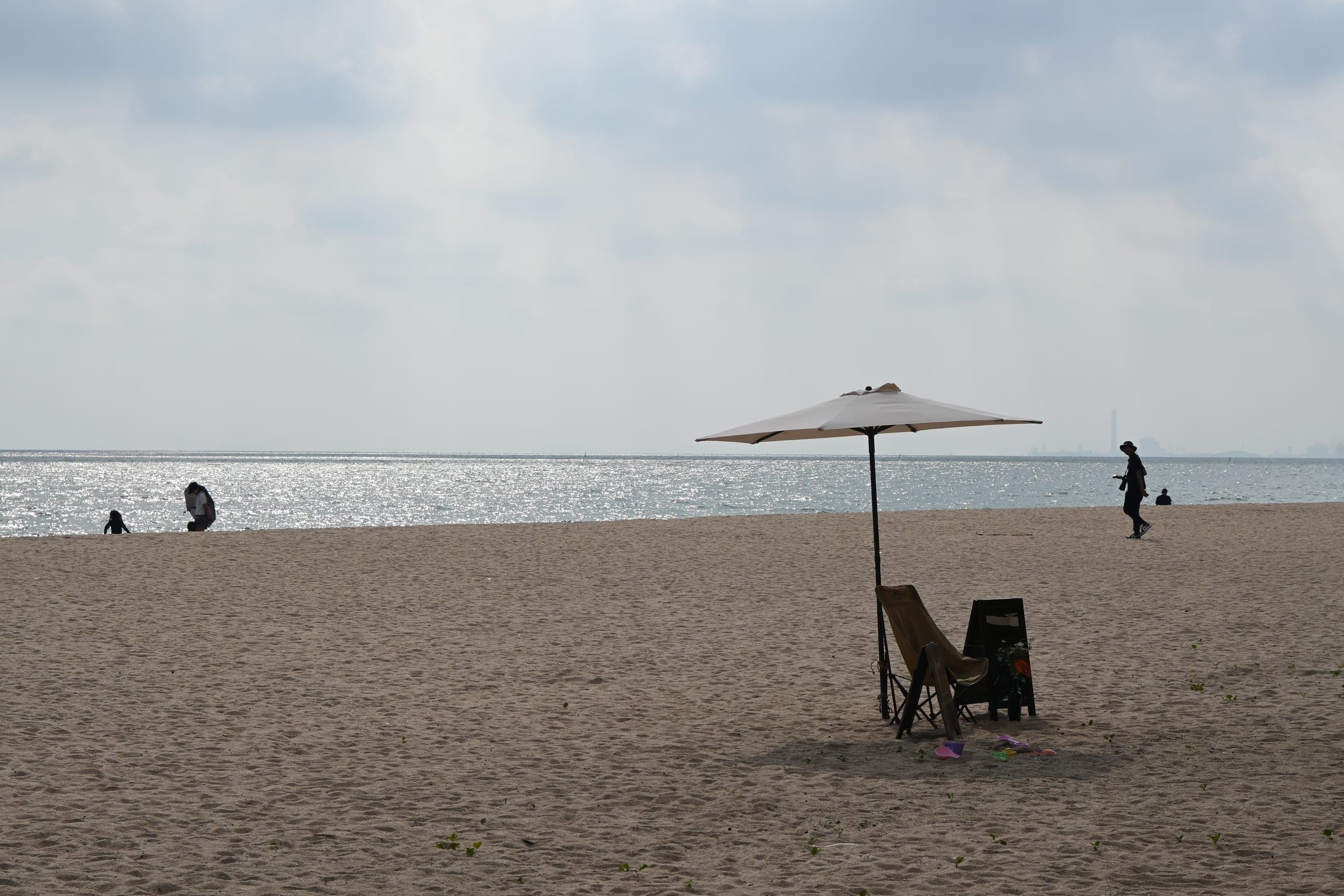 A beach umbrella and two chairs on quiet sunlit sand with a few distant walkers
