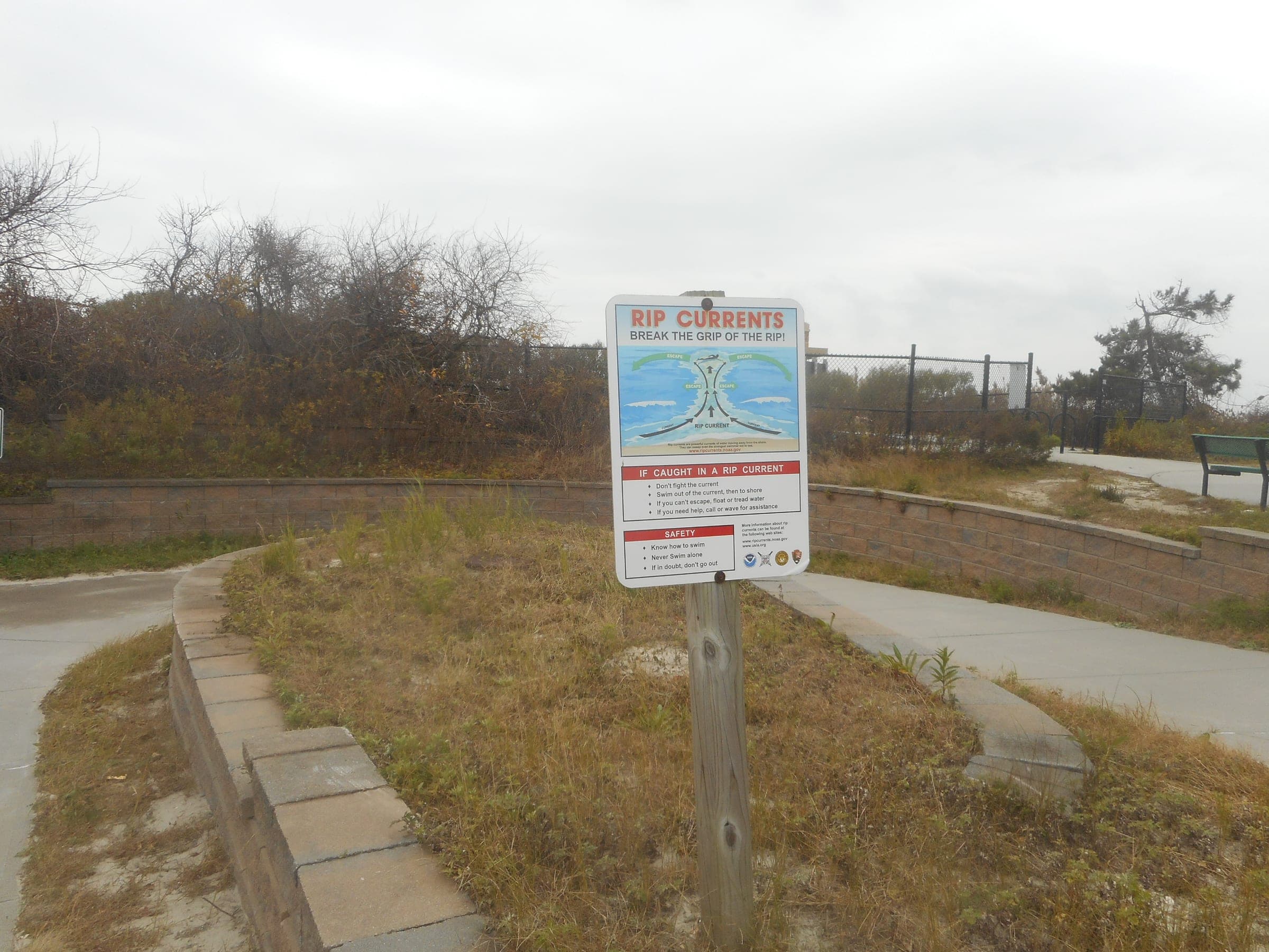 A rip current warning sign at a beach access path